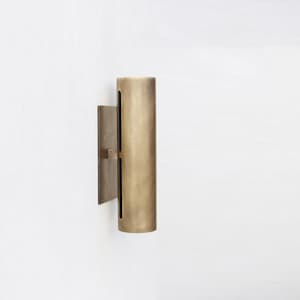 May include: A cylindrical wall sconce with a brushed brass finish. The sconce has a rectangular backplate and a vertical, slotted design. The fixture is mounted on a white wall, showcasing a minimalist aesthetic.