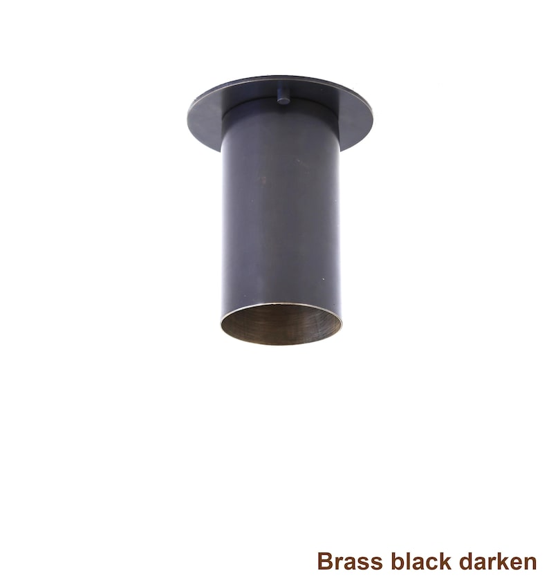 May include: A cylindrical ceiling light fixture with a dark, matte black finish on the exterior and a metallic brass interior rim. The fixture features a flat, circular mounting plate at the top. The text "Brass black darken" is visible below.