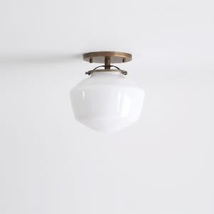 May include: A flush mount ceiling light fixture featuring a smooth, white, schoolhouse-style glass globe shade attached to a circular, antique brass-finished metal canopy with a short central stem and three small decorative mounting screws.