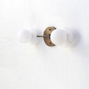 May include: A brass wall sconce with three white globe light fixtures. The sconce has a circular base and a metal arm that extends to the side.