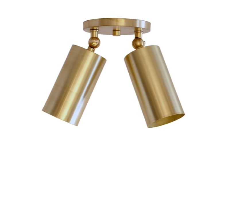 Op de afbeelding: Een plafondlamp met twee koppen, voorzien van een ronde messing montageplaat en twee cilindrische spots. Elke lichtkop is met een draaikoppeling aan de basis bevestigd, waardoor de goudkleurige lampen in verschillende standen verstelbaar zijn.