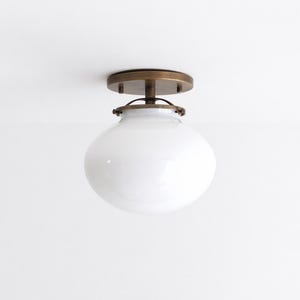 May include: A flush mount ceiling light fixture featuring a round, opaque white glass globe shade attached to a circular, dark brass-toned metal canopy. The metal hardware includes a central stem and a decorative frame that secures the glass shade.
