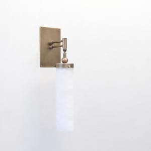 May include: A wall-mounted light fitting featuring a rectangular brass backplate with an adjustable double-jointed arm and a spherical pivot point. The light includes a cylindrical, translucent white glass shade with a subtle marbled texture.