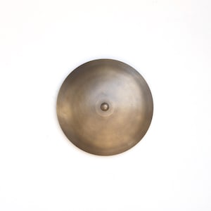 May include: A round, brass-colored ceiling light fixture with a slightly domed shape. The light has a small, round, metal center.