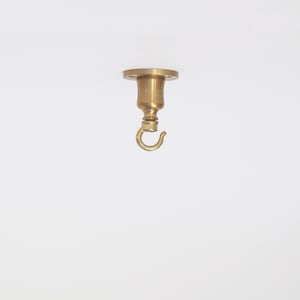 May include: A brass ceiling hook with a circular base and a curved hook. The hook is designed for hanging items from the ceiling. The fixture has a vintage aesthetic and is made of a shiny, golden metal.