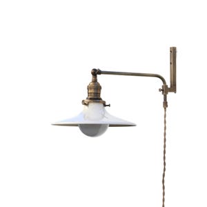 May include: A vintage-style wall-mounted lamp with a white, conical shade and a brass-colored arm. The lamp features a clear bulb and a twisted brown cord. The design evokes an industrial or farmhouse aesthetic.