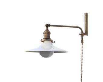 May include: A vintage-style wall-mounted lamp with a white, conical shade and a brass-colored arm. The lamp features a clear bulb and a twisted brown cord. The design evokes an industrial or farmhouse aesthetic.