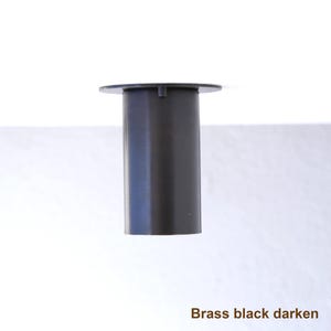 May include: A cylindrical black brass component featuring a flat circular top plate with a small protruding tab. The object has a smooth, matte finish and is labeled with the text Brass black darken at the bottom right corner of the image.