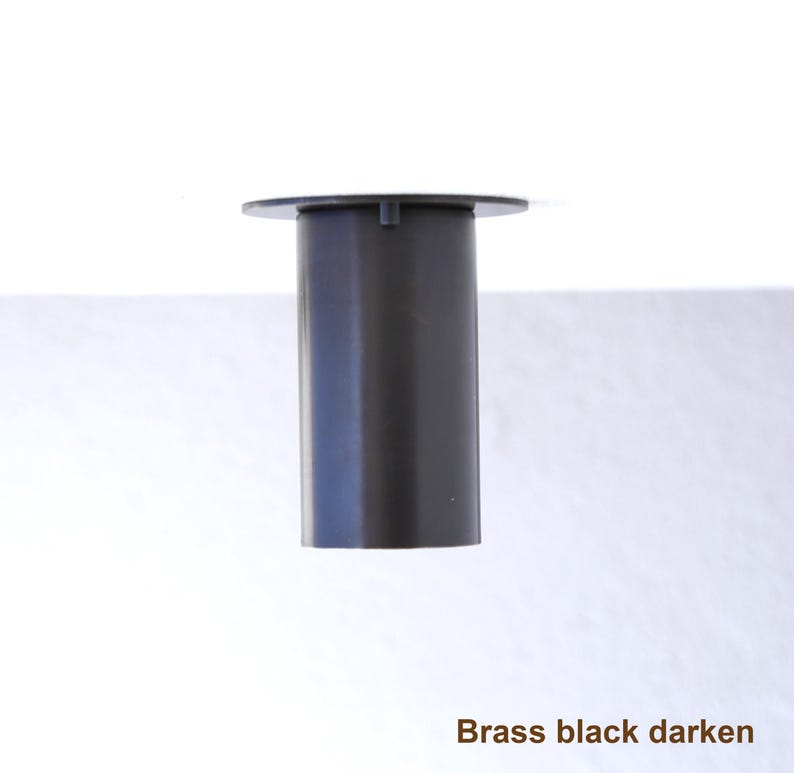 May include: A cylindrical black brass component featuring a flat circular top plate with a small protruding tab. The object has a smooth, matte finish and is labeled with the text Brass black darken at the bottom right corner of the image.