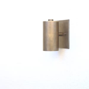 May include: A brass wall sconce with a cylindrical shade and a square backplate.