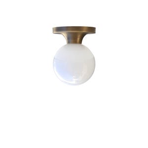 May include: A modern flush mount ceiling light fixture. It features a round, white glass globe shade and a brass-colored metal base. The fixture is designed for indoor use and provides ambient lighting.
