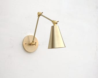 Könnte beinhalten: Eine goldfarbene Wandleuchte mit einem konischen Schirm und einem verstellbaren Arm.
