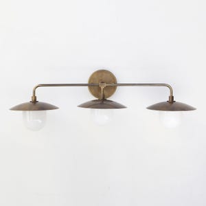 May include: A brass wall sconce with three lights. Each light has a round, frosted glass globe and a curved, brass shade.