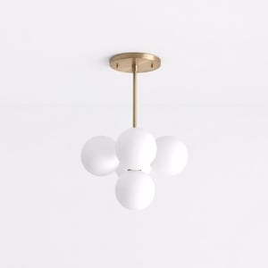 May include: A ceiling light fitting featuring a circular brass canopy and a central rod that supports four spherical, frosted white glass globes arranged in a cluster. The metal components have a smooth, brushed brass finish throughout the structure.