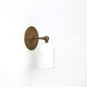 May include: A brass wall sconce with a white ceramic shade. The sconce has a round back plate and a single bulb.