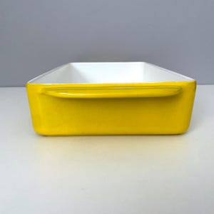 Op de afbeelding: Een rechthoekige ovenschaal met een heldergele buitenkant en een witte binnenkant. De schaal heeft aan elke kant een handvat. Het ontwerp is eenvoudig en modern, geschikt om in te bakken en te serveren.