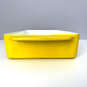 Op de afbeelding: Een rechthoekige, heldergele keramische ovenschaal met een witte binnenkant. De schaal heeft aan elke kant een handvat. Ideaal om in te bakken en te serveren. Witte en grijze achtergrond.
