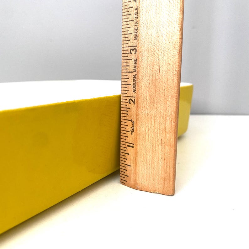 Op de afbeelding: Een rechthoekige, gele keramische schaal met een witte binnenkant. Een houten liniaal, gemarkeerd in inches, wordt naast de schaal geplaatst. De liniaal is gemarkeerd met de tekst "Made in U.S.A."