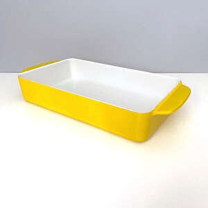 Op de afbeelding: Een rechthoekige ovenschaal met een heldergele buitenkant en een witte binnenkant. De schaal heeft afgeronde handvatten aan elk uiteinde. Dit keukengerei is geschikt voor het bakken van ovenschotels, desserts en andere gerechten.