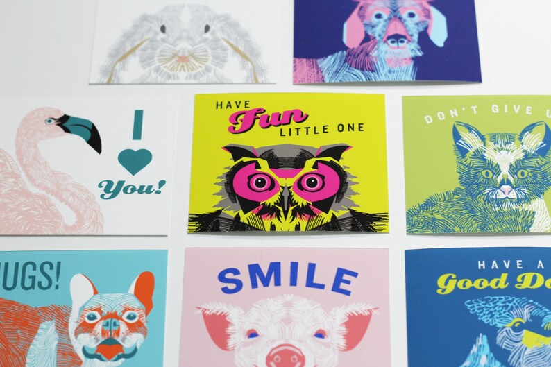 May include: Set of eight greeting cards featuring colorful illustrations of animals with text. The cards include a flamingo, a rabbit, a dog, an owl, a cat, a pig, a bulldog, and a zebra. The text on the cards includes "I love you!", "Have Fun Little One", "Don't Give Up", "Smile", "Have a Good Day", and "Hugs!"