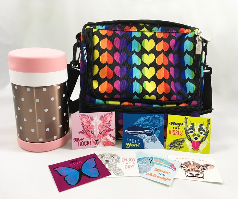 May include: A black lunch bag with a rainbow heart pattern. The bag has a zipper closure and a top handle. There are several small cards with encouraging messages and illustrations of animals, including a fox, a bird, a dog, and a cow.