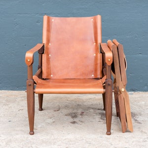 May include: A brown leather chair with wooden arms and legs. The chair is folded and has a wooden frame.