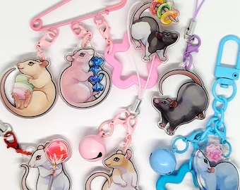 May include: A collection of colorful rat-themed charms. Each charm features a different rat design, some holding treats like candy and marshmallows. The charms are attached to various accessories, including keychains, safety pins, and lanyards. The color palette includes pink, blue, and pastel tones.