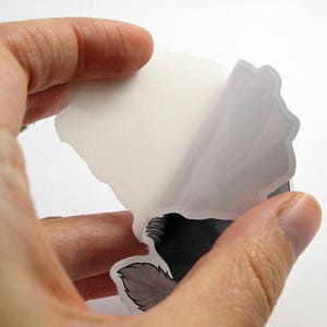 May include: A sticker with a black and white illustration of a wolf's head. The sticker is being peeled off of a white backing.