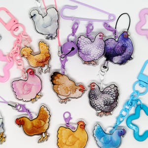 May include: A collection of chicken-themed keychains and charms in various colors, including white, yellow, pink, and blue. Each charm features a detailed illustration of a chicken and is attached to a chain or clasp.