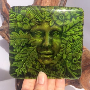 Puede incluir: Pieza de arte de vidrio verde que representa el rostro de una mujer rodeado de hojas y flores. La pieza tiene un efecto texturizado en 3D.