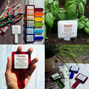 May include: A selection of colourful garden plant markers. Each marker features a rectangular label with the plant name and botanical details. The markers are in various colours, including red, green, blue, and yellow. The image also shows gardening tools and plants.