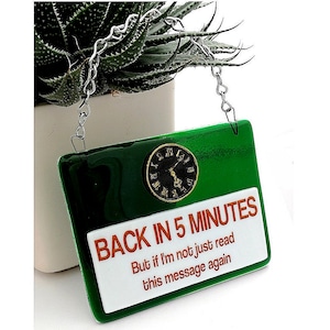 Puede incluir: Un letrero verde con letras blancas que dice "Back in 5 minutes. But if I'm not just read this message again." Un reloj de cara con números romanos está en la esquina superior izquierda del letrero.