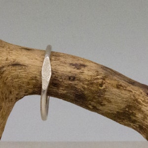 Könnte beinhalten: Ein silberner Ring mit einem strukturierten, diamantförmigen Band.