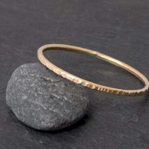 K&ouml;nnte beinhalten: Ein d&uuml;nner Goldring mit geh&auml;mmerter Textur. Der Ring liegt auf einem grauen Stein.