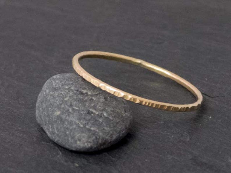 K&ouml;nnte beinhalten: Ein d&uuml;nner Goldring mit geh&auml;mmerter Textur. Der Ring liegt auf einem grauen Stein.