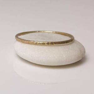 K&ouml;nnte beinhalten: Ein d&uuml;nner goldener Ring mit geh&auml;mmerter Textur, der auf einem wei&szlig;en Stein liegt.
