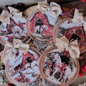 May include: Five circular ornaments featuring winter scenes with white horses, red barns, and snow. Each ornament is topped with a beige fabric bow and accented with a silver metal filigree piece at the bottom, finished with a beaded border.