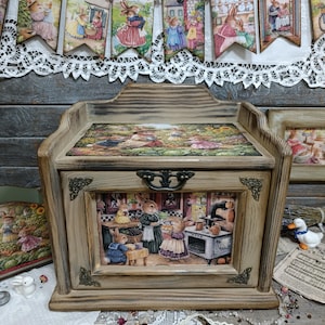 May include: A wooden bread box with a decorative bunny scene on the front and top. The box has a light brown finish with dark brown accents. A banner of bunny illustrations hangs above the box.