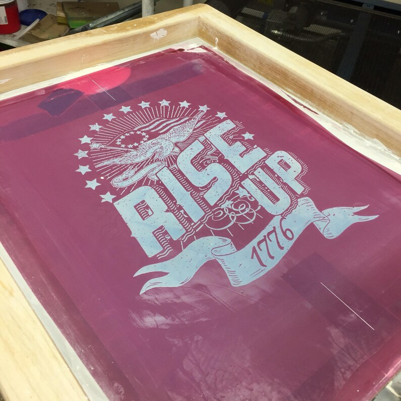 Peut inclure: Un cadre de s&eacute;rigraphie avec un fond rouge et un motif bleu et blanc qui dit "Rise Up 1776". Le motif repr&eacute;sente un aigle, des &eacute;toiles et une banni&egrave;re.