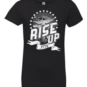 Peut inclure: T-shirt noir avec un motif graphique blanc repr&eacute;sentant un drapeau am&eacute;ricain stylis&eacute;, des &eacute;toiles et le texte "Rise Up 1776".