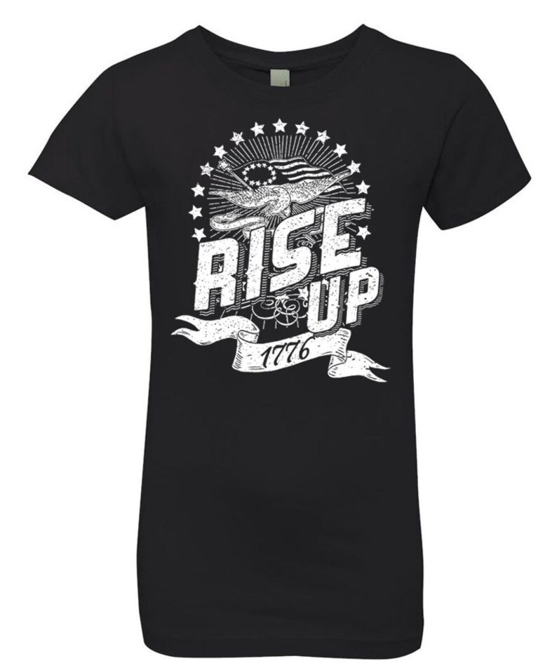Peut inclure: T-shirt noir avec un motif graphique blanc repr&eacute;sentant un drapeau am&eacute;ricain stylis&eacute;, des &eacute;toiles et le texte "Rise Up 1776".