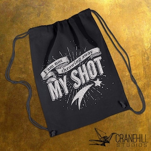 May include: Black drawstring bag with the text "I am not throwing away my shot" in white. The bag has a star and shooting star design. The Cranehill Studios logo is in the bottom right corner.
