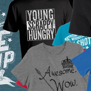 Peut inclure: Une collection de six t-shirts avec diff&eacute;rents motifs et slogans. Les t-shirts pr&eacute;sentent un motif bleu et blanc avec le texte "Rise Up 1776", un t-shirt noir avec le texte "Young Scrappy Hungry", un t-shirt bleu avec le texte "I am not throwing away my shot", un t-shirt gris avec le texte "Awesome. Wow." et une couronne, un t-shirt bleu avec le texte "Feel the Burr 1800 Gonna be in the room where it happens", et un t-shirt rouge, blanc et bleu avec le texte "I am not throwing away my shot".