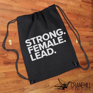 May include: Black drawstring bag with white text that reads "STRONG. FEMALE. LEAD."