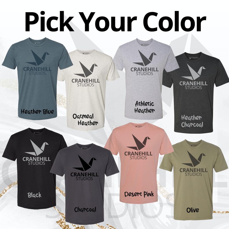 May include: A selection of t-shirts in various colours, each featuring a grey origami crane logo with the text "Cranehill Studios". The colours include heather blue, oatmeal heather, athletic heather, heather charcoal, black, desert pink, charcoal, and olive.