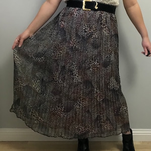 May include: A long, pleated skirt with a black and brown leopard print. The skirt is made of a sheer fabric and has a black belt.