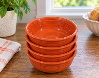 May include: A stack of four vibrant orange ceramic bowls with a glossy finish and concentric ring detailing on the interior base. Each bowl features a rounded shape and a smooth, uniform surface, creating a consistent vertical stack.