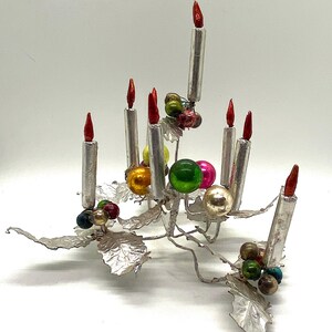 May include: Silver Christmas tree centrepiece with seven silver candles and colourful glass baubles. The base of the centrepiece is made of silver leaves.