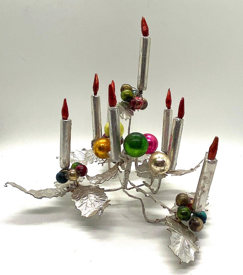 May include: Silver Christmas tree centrepiece with seven silver candles and colourful glass baubles. The base of the centrepiece is made of silver leaves.