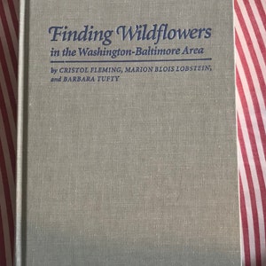 May include: A green book with the title "Finding Wildflowers in the Washington-Baltimore Area" by Cristol Fleming, Marion Blois Lobstein, and Barbara Tufty.